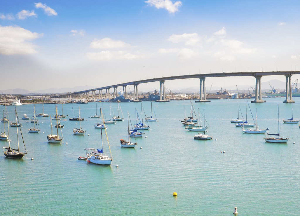 Lots of sailboats on harbor with large grey bridge in the background